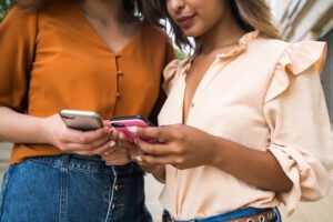 portrait two young friends enjoying together using their mobile phones while standing outdoors urban concept