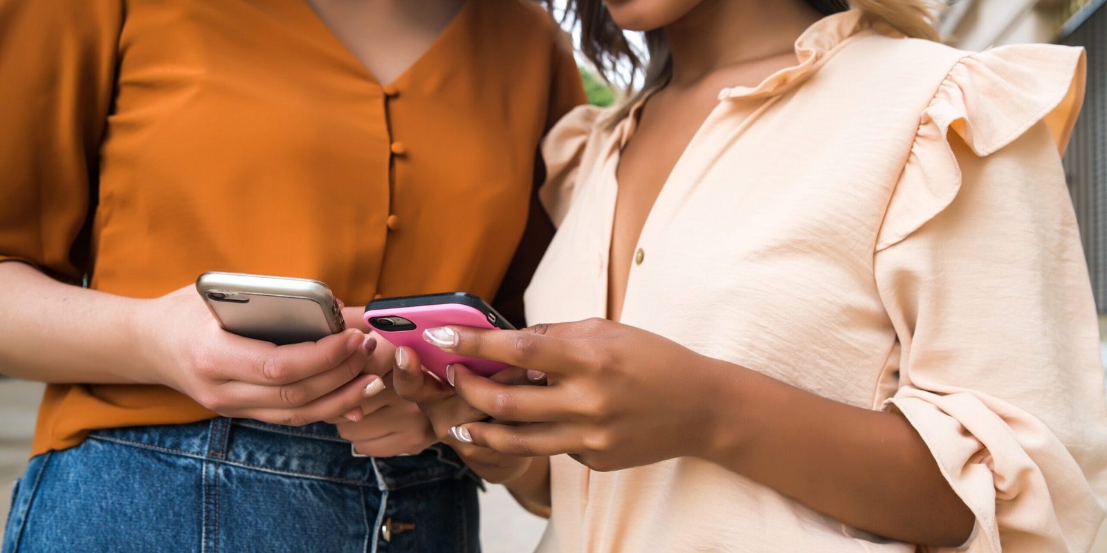Two friends using mobile phone outdoors.